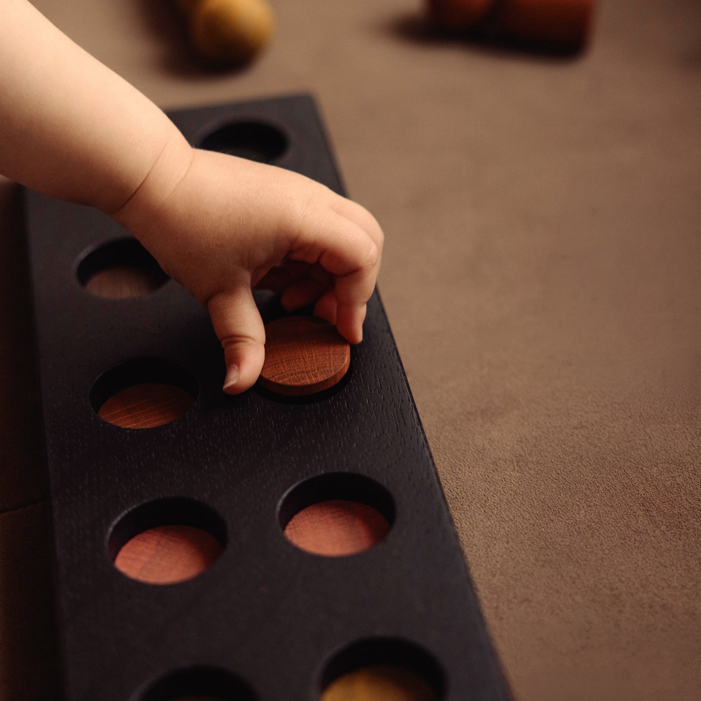 Montessori-inspired wooden pegboard toy in Black Oak with Earth Palette by Woodsie Wonder, shown in close-up play detail with a child’s hand.