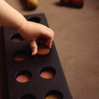 Montessori-inspired wooden pegboard toy in Black Oak with Earth Palette by Woodsie Wonder, shown in close-up play detail with a child’s hand.