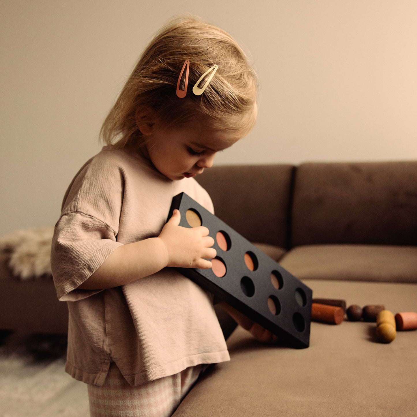 Play & Hang wooden colour sorting toy and children’s wall coat rack in one by Woodsie Wonder. Shown in Black Oak with Earth Palette as a child plays and matches the wooden pegs.