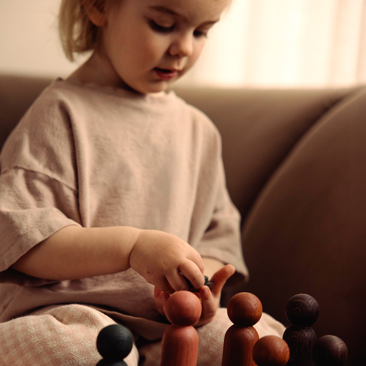 Play & Hang wooden colour sorting toy and children’s wall coat rack in one by Woodsie Wonder. Shown in Brown Oak with Earth Palette as a child plays and matches the wooden pegs.