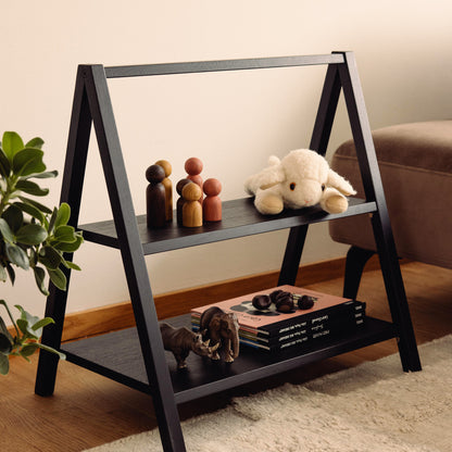 Wooden kids' book and toy shelf in a living room setting, made of FSC-certified solid oak. Play & Read in Black Oak by Woodsie Wonder.