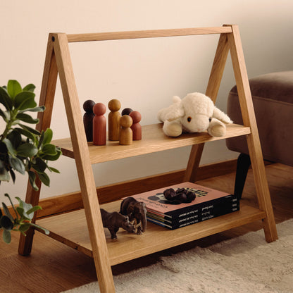 Wooden kids' book and toy shelf in a living room setting, made of FSC-certified solid oak. Play & Read in Natural Oak by Woodsie Wonder.