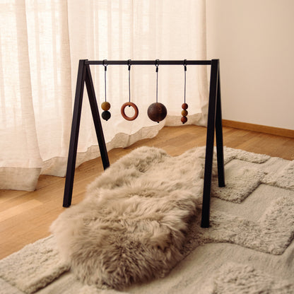 Wooden baby play gym with hanging toys that transforms into elegant bookshelf. Play & Read in Black Oak with Earth Palette by Woodsie Wonder.