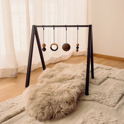 Wooden baby play gym with hanging toys that transforms into elegant bookshelf. Play & Read in Black Oak with Mono Palette by Woodsie Wonder.