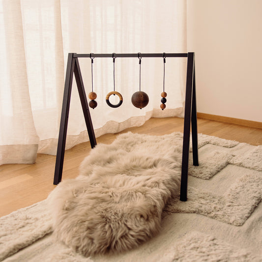 Wooden baby play gym with hanging toys that transforms into elegant bookshelf. Play & Read in Black Oak with Mono Palette by Woodsie Wonder.