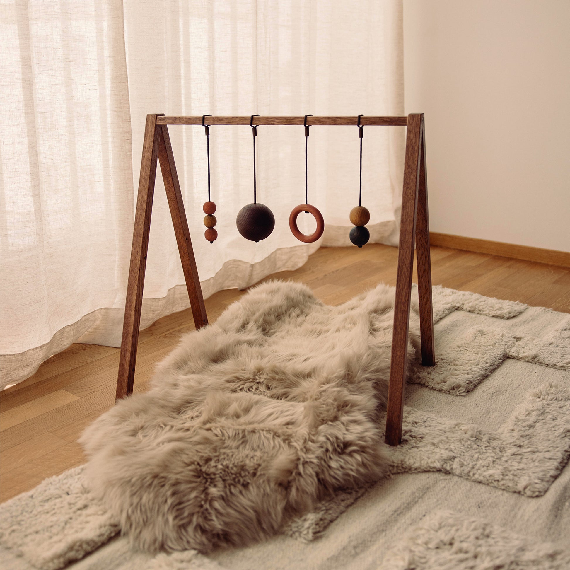 Wooden baby play gym with hanging toys that transforms into a children's bookshelf. Play & Read in Brown Oak with Earth Palette by Woodsie Wonder.