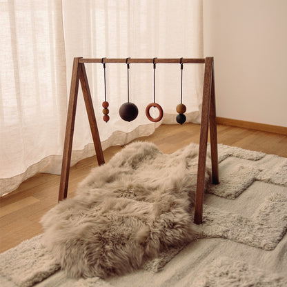 Wooden baby play gym with hanging toys that transforms into a children's bookshelf. Play & Read in Brown Oak with Earth Palette by Woodsie Wonder.