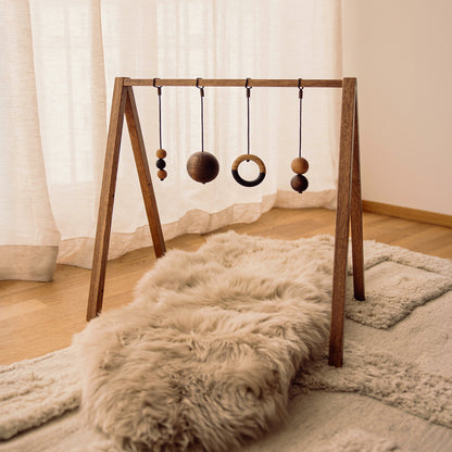 Wooden baby play gym with hanging toys that transforms into a children's bookshelf. Play & Read in Brown Oak with Mono Palette by Woodsie Wonder.