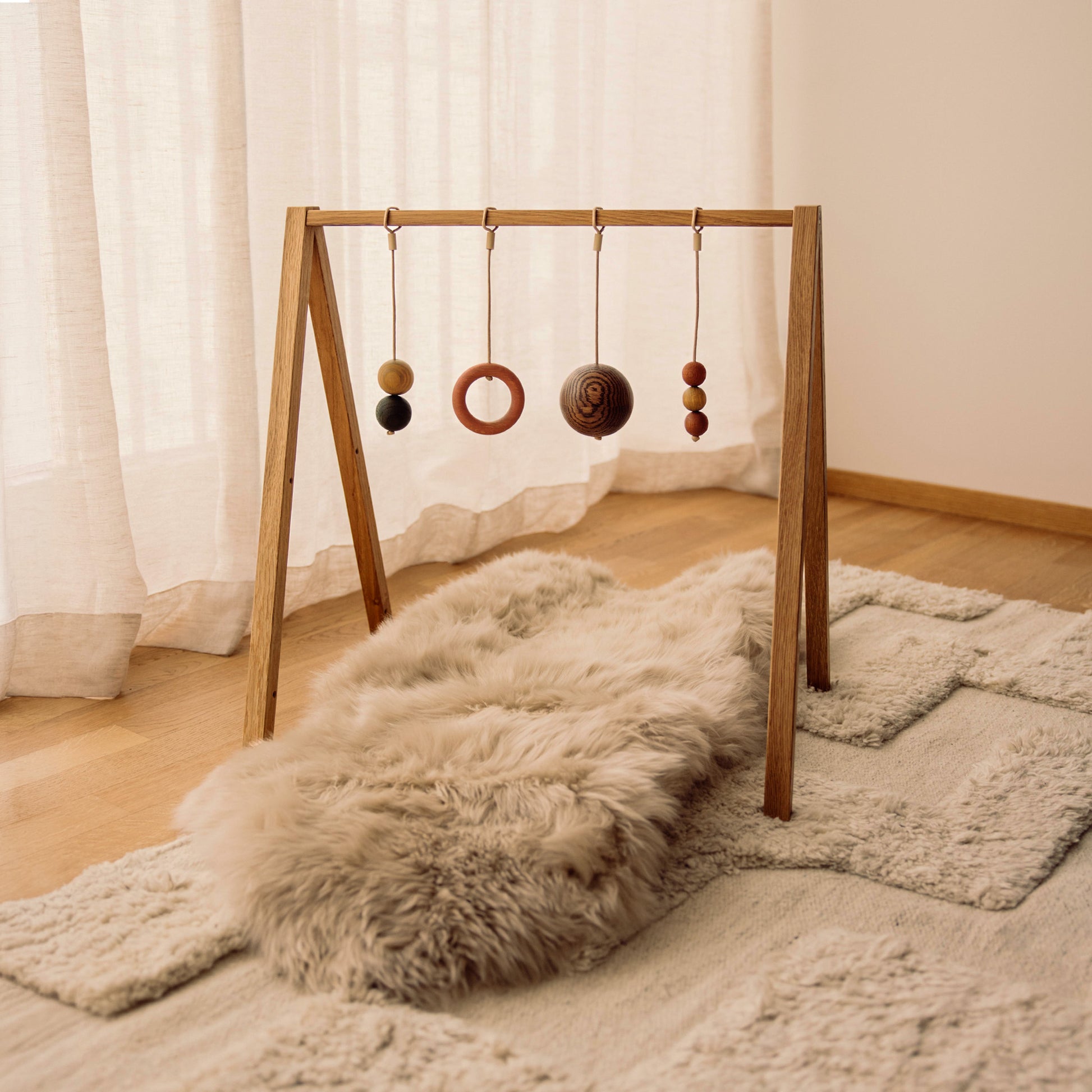 Wooden baby play gym with hanging toys that transforms into elegant bookshelf. Play & Read in Natural Oak with Earth Palette by Woodsie Wonder.