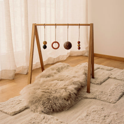 Wooden baby play gym with hanging toys that transforms into elegant bookshelf. Play & Read in Natural Oak with Earth Palette by Woodsie Wonder.