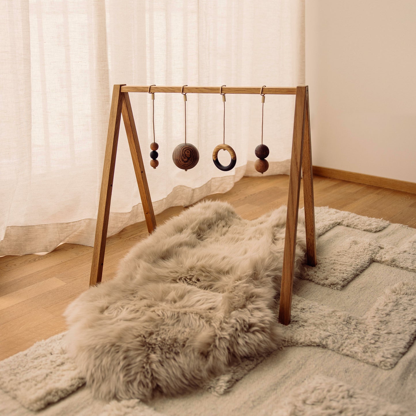 Wooden baby play gym with hanging toys that transforms into elegant bookshelf. Play & Read in Natural Oak with Mono Palette by Woodsie Wonder.