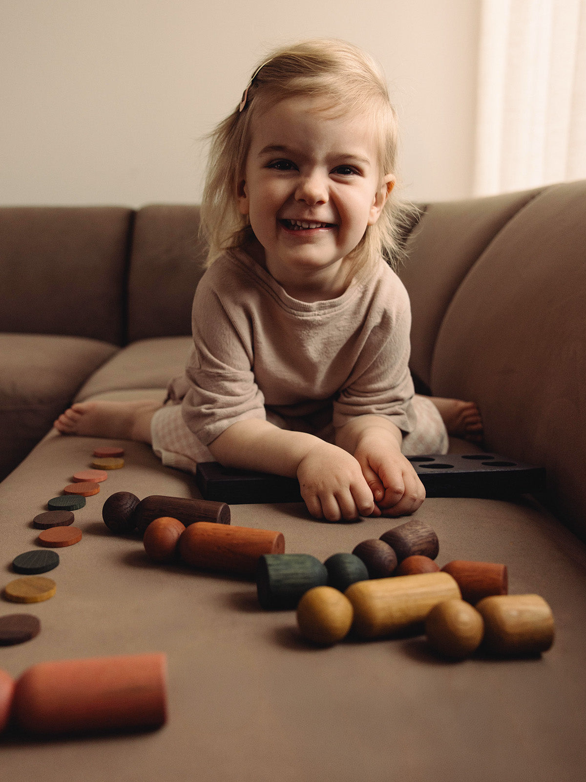 Play & Hang wooden sorting toy that transforms into a coat rack by Woodsie Wonder, shown with a child playing in a modern family interior.